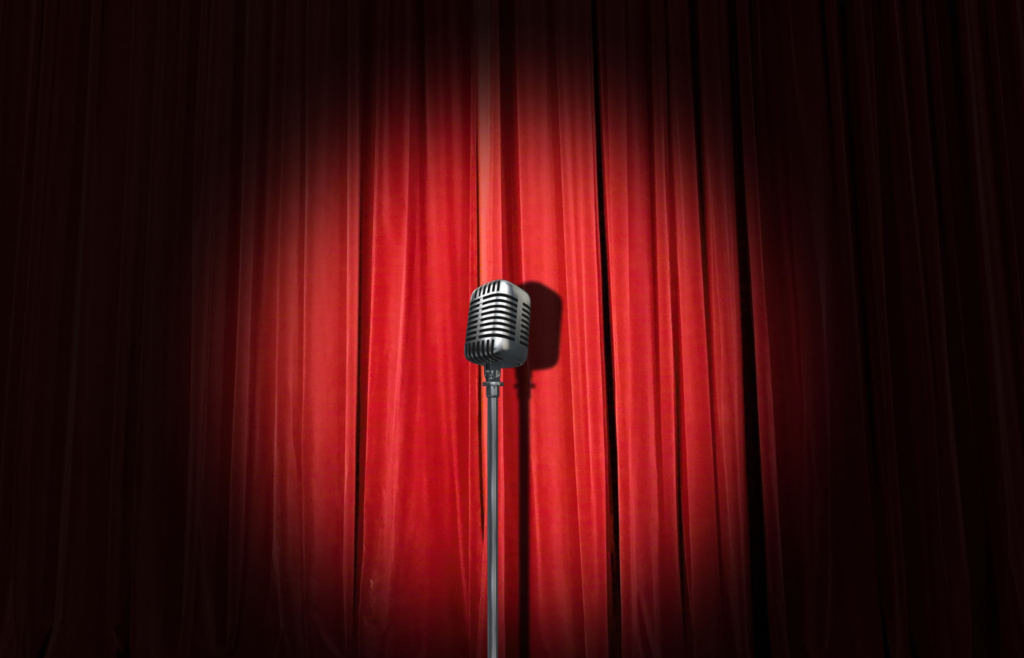 comedy stage and microphone against a red curtain and spotlight