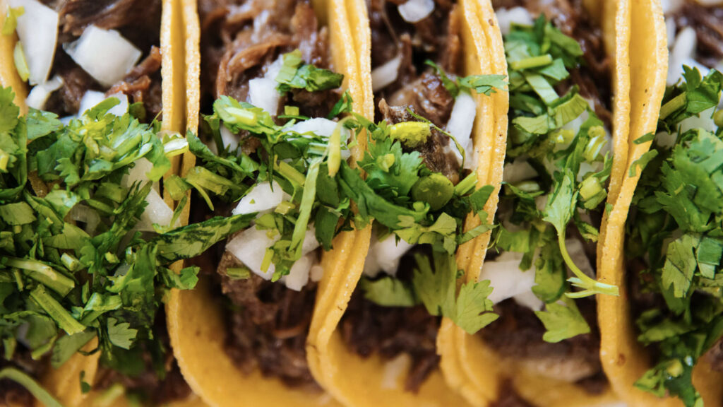 Row of tacos with cilantro and onions